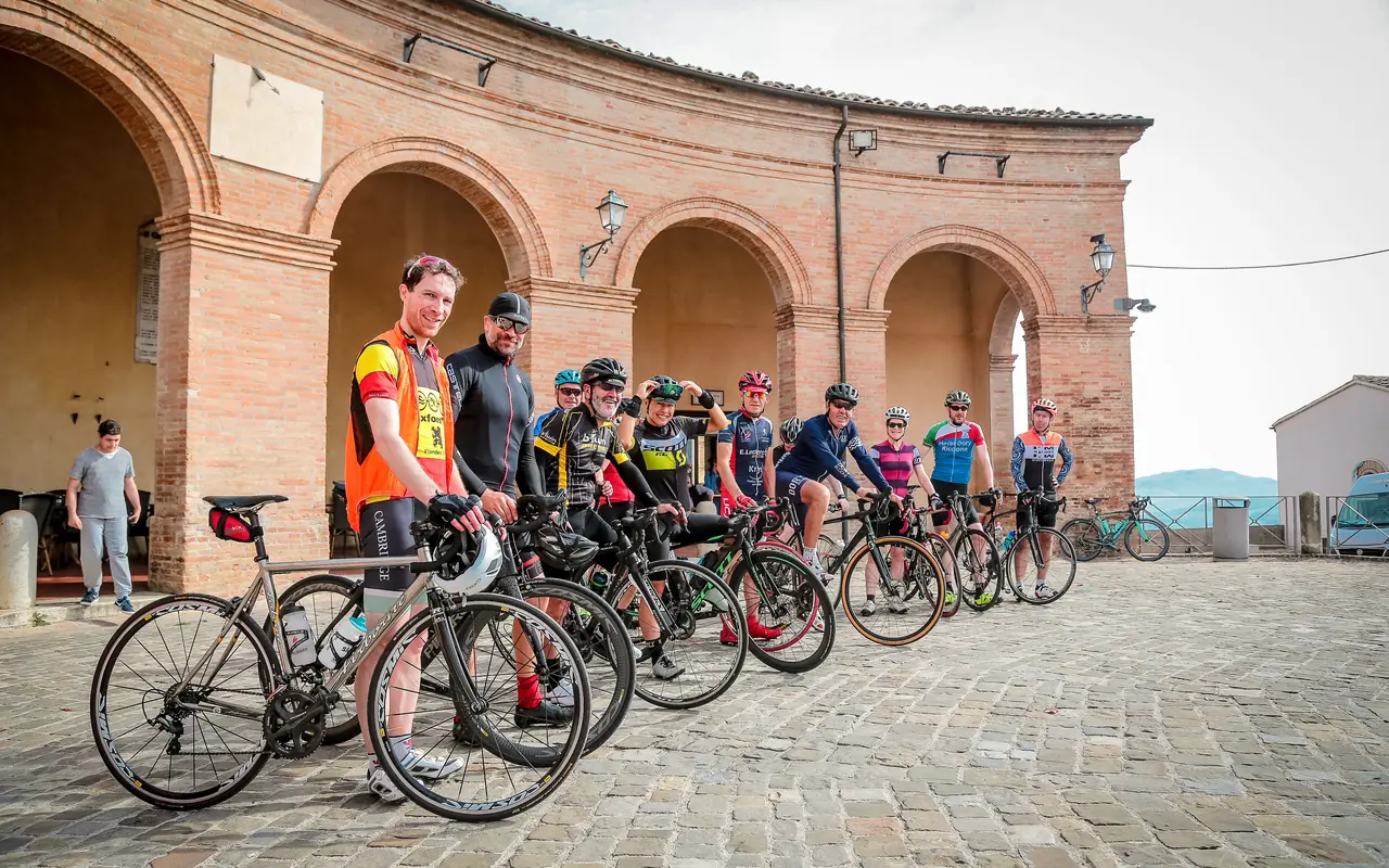 Gruppo di ciclisti in sosta con le bici da corsa sotto il portico di Piazza Maggiore a Mondaino